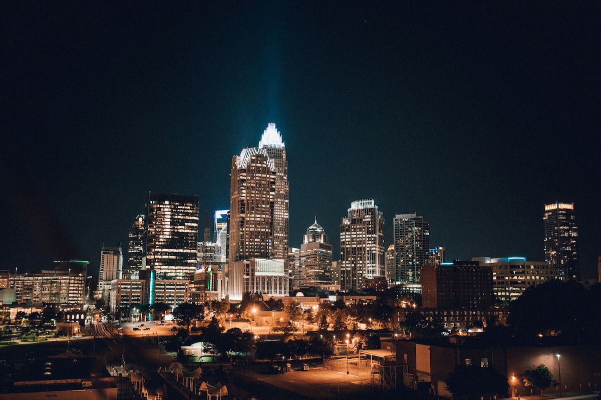 Charlotte, North Carolina skyline at night, featuring the illuminated Bank of America Corporate Center and surrounding high-rise buildings glowing against the dark sky.