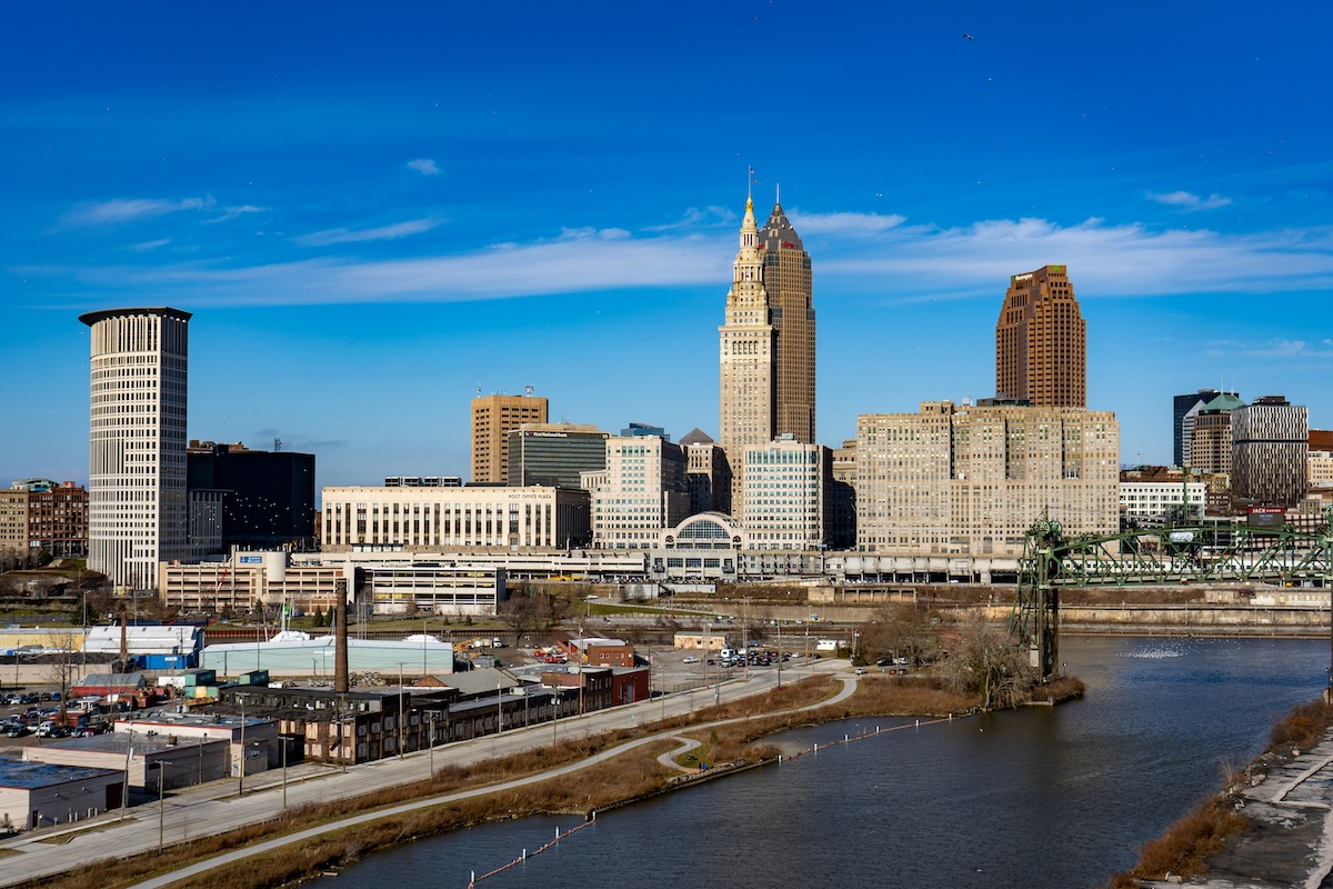 Downtown Cleveland skyline with the Terminal Tower and Key Tower rising above surrounding buildings, viewed from across the Cuyahoga River under a clear blue sky.
