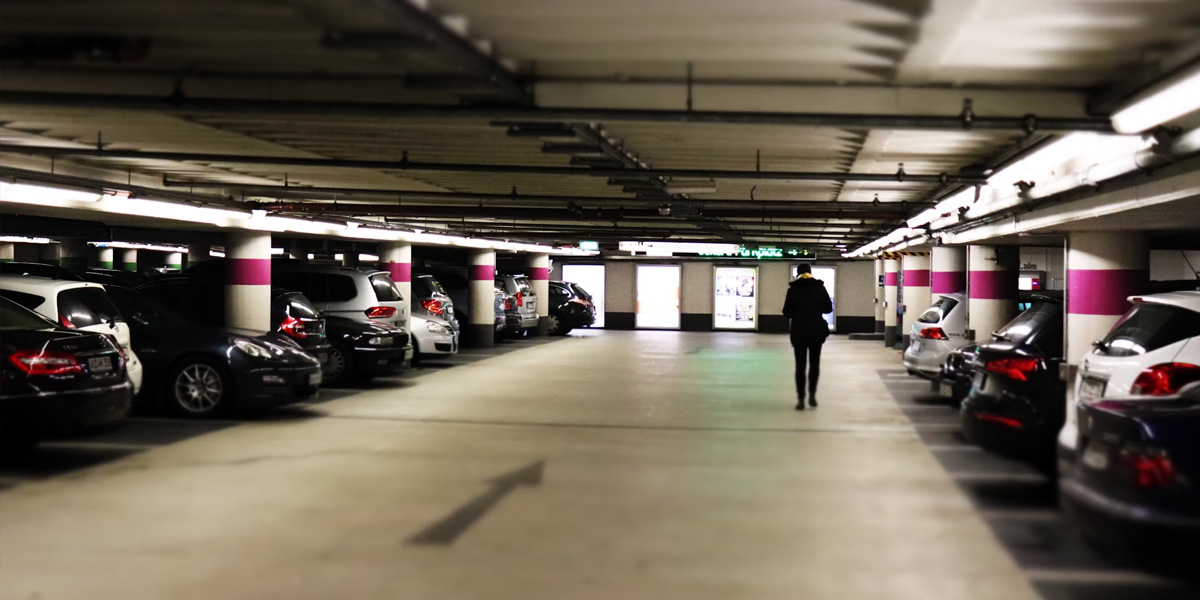 Close-up of parked cars in an indoor parking garage, with a person walking toward the building.
