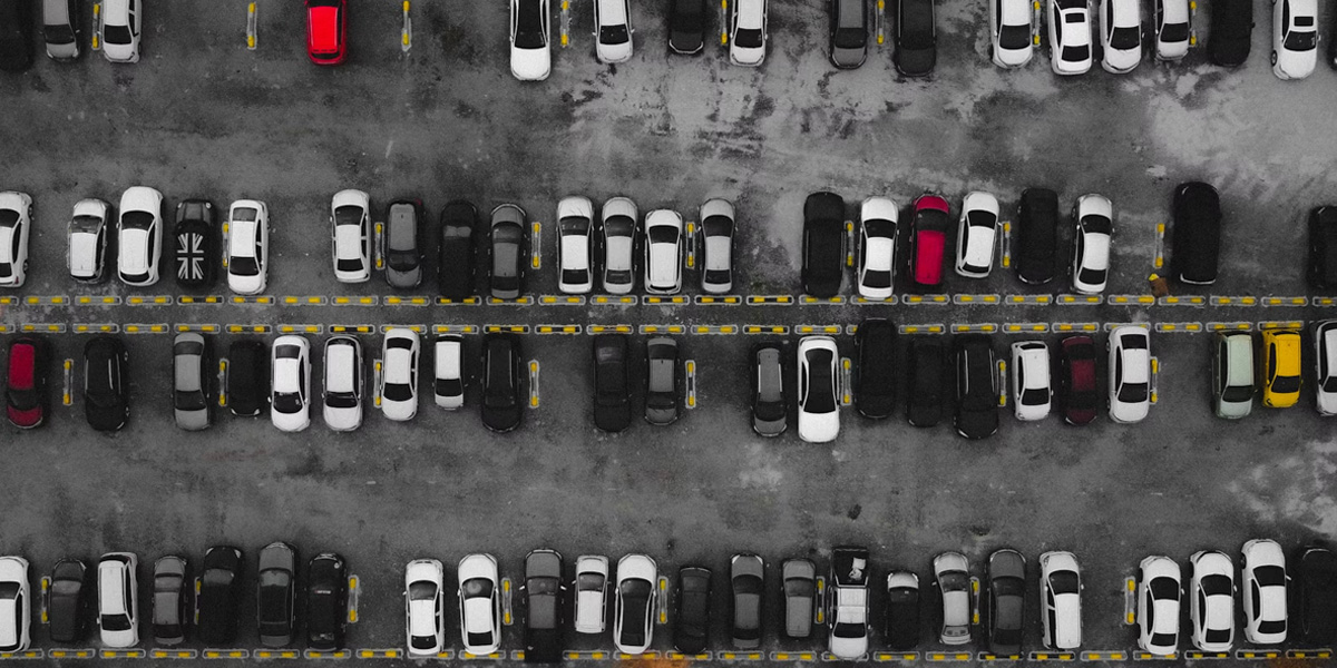 Aerial view of a snowy outdoor parking lot with rows of black, white, and a few red cars parked between yellow dividers.