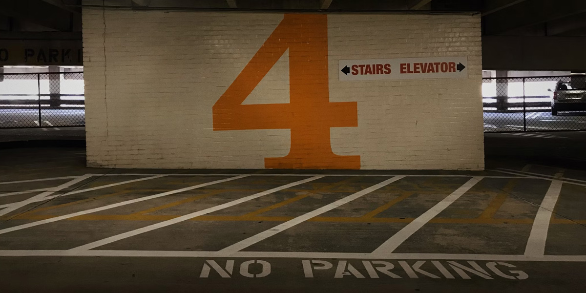 Inside a parking garage showing a large orange number 4 painted on a wall with directional arrows for stairs and elevator, and 'No Parking' marked on the ground.