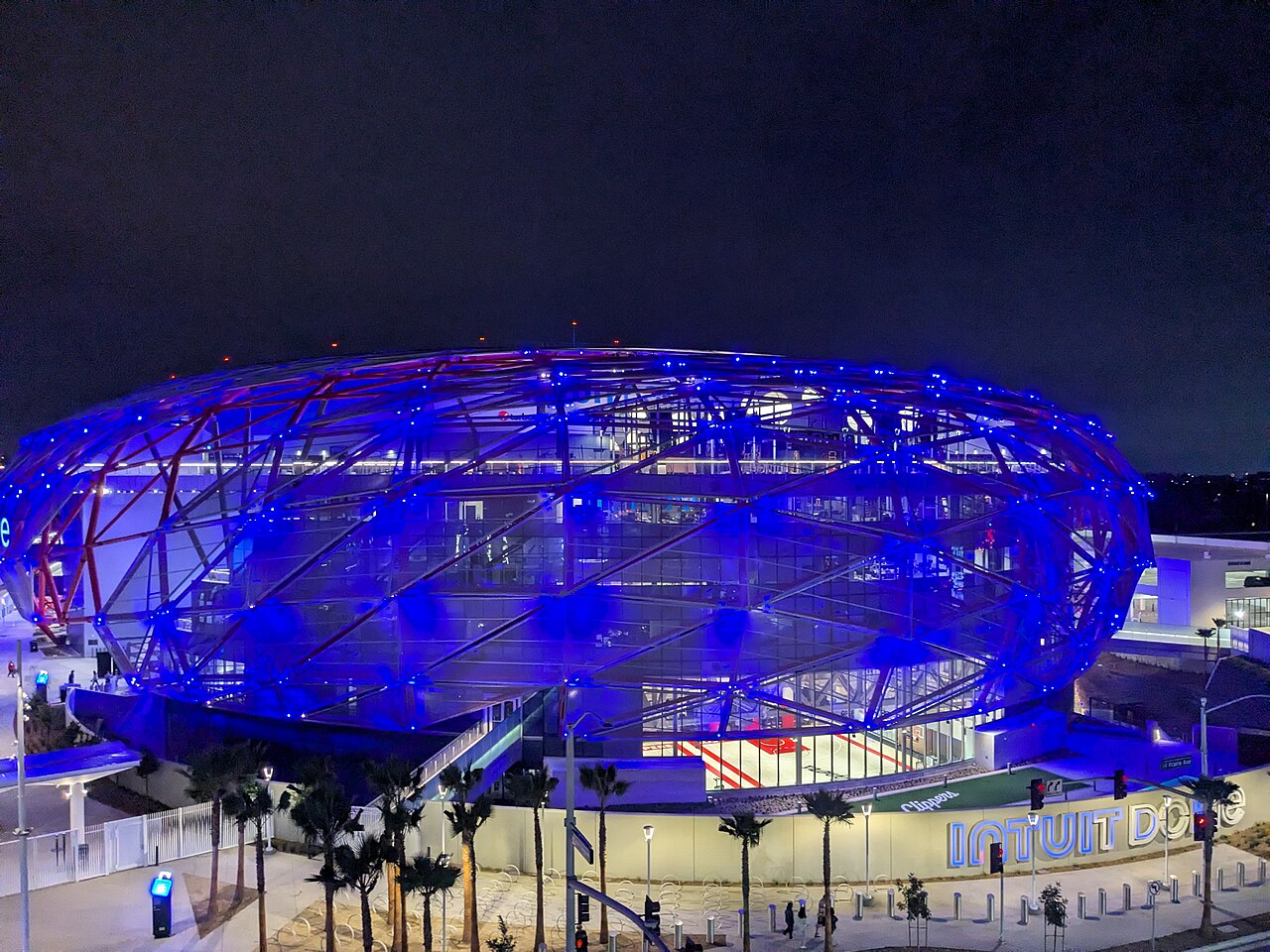Intuit Dome as seen in the distance glowing blue or purple at night. Image courtesy Wikimedia Commons.