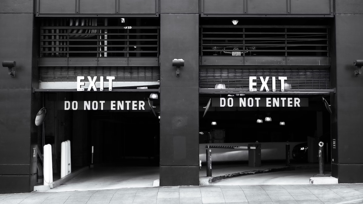 Black and white photo of a parking garage exit with two lanes marked “EXIT” and large “DO NOT ENTER” signs above each lane.